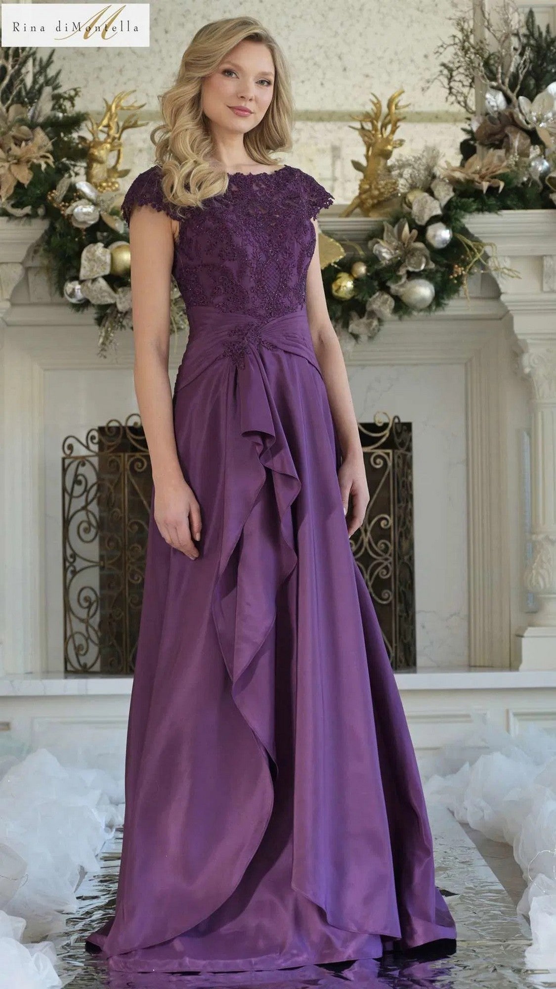 A woman stands indoors in the Long Formal Dress: Rina Di Montella RD3327, featuring a lace-embroidered bodice and floor-length light aubergin satin skirt, surrounded by floral decorations and ornaments in the background.